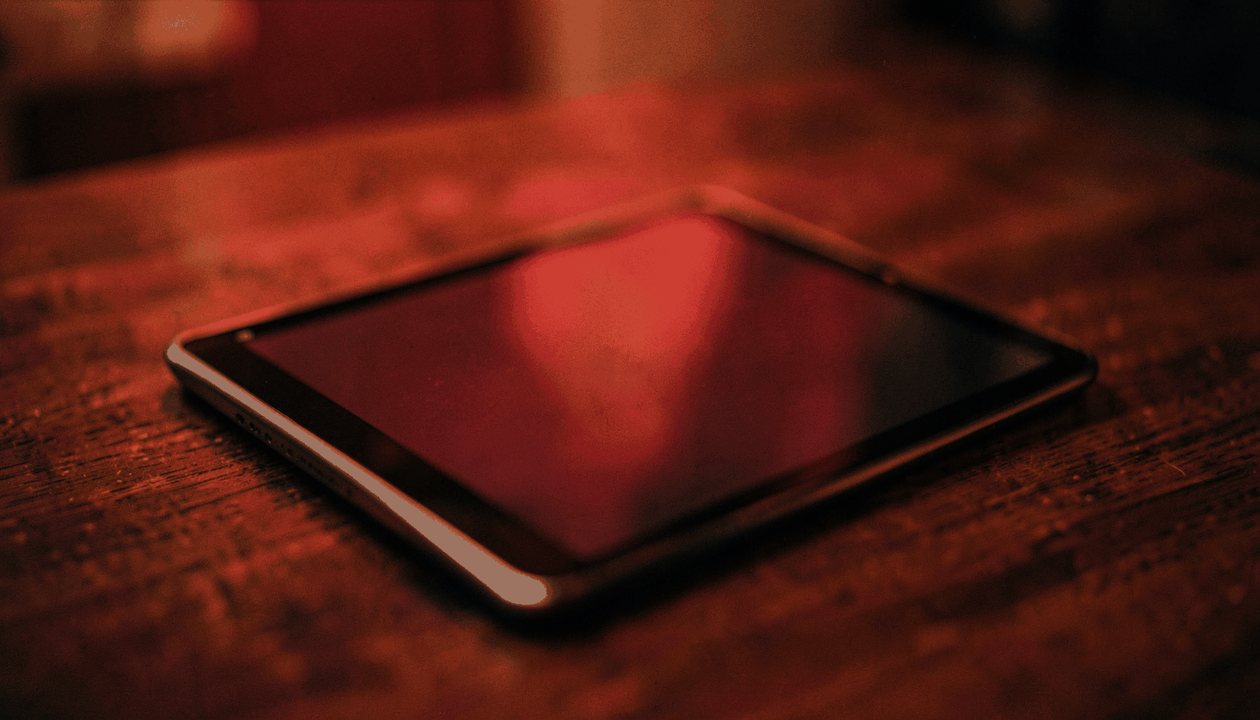 A softly lit digital tablet resting on a dark wooden surface, warm ambient glow with shallow depth of field, cinematic wide frame